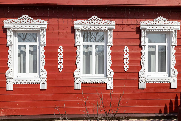 Trois fenêtres avec des plates-bandes blanches sculptées sur le mur rouge d'un vieux manoir russe en bois. - Photo, image