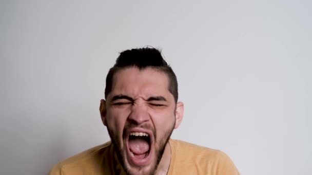Jonge knappe Europese blanke man met baard schreeuwt nee en grijpt zijn hoofd met beide handen. Persoon toont de emoties van woede op een witte achtergrond. - Video