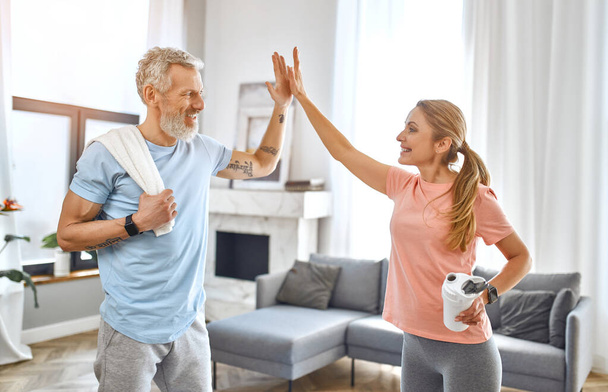 Sport, fitness és egészséges életmód koncepció. Idős pár ad öt gesztus, és nem gyakorlatok otthon, és érezd jól magad. Hogyan maradjunk egészségesek a karanténban?. - Fotó, kép