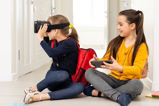 volledige weergave van twee multiculturele schoolmeisjes hand in hand terwijl het gebruik van virtial reality headsets op witte achtergrond - Foto, afbeelding