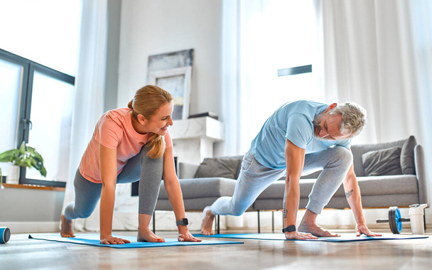 Spor, spor ve sağlıklı yaşam tarzı konsepti. Yetişkin bir çift evde egzersiz ya da yoga yapıyor. Karantinada nasıl sağlıklı kalınır?. - Fotoğraf, Görsel
