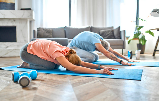 Sport, fitness en een gezonde levensstijl concept. Volwassen stel doet aan lichaamsbeweging of yoga thuis. Hoe gezond te blijven in quarantaine. - Foto, afbeelding