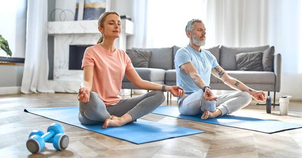 Sport, fitness and healthy lifestyle concept. Mature couple doing exercise or yoga at home. How to stay healthy in quarantine. - Photo, Image