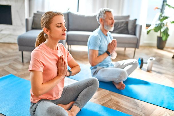 Sport, fitness and healthy lifestyle concept. Mature couple doing exercise or yoga at home. How to stay healthy in quarantine. - Photo, Image