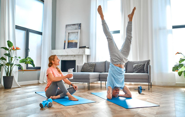 Sport, fitness en een gezonde levensstijl concept. Volwassen echtpaar doen oefening of yoga thuis en plezier hebben. Hoe gezond te blijven in quarantaine. - Foto, afbeelding