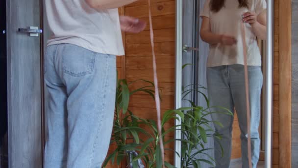 Sección media de esbelta hembra de 30 años midiendo su cintura con cinta adhesiva y mirando a su propio reflejo en el espejo en casa - Metraje, vídeo