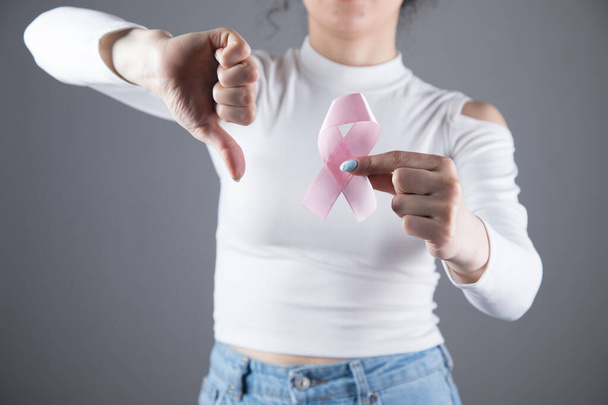 young girl holds a pink ribbon showing her thumb down on a gray background - Fotoğraf, Görsel