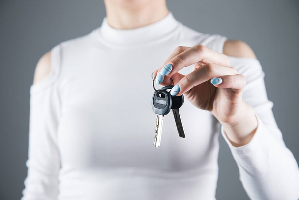 young woman holds the keys to the house on a gray background - Photo, Image