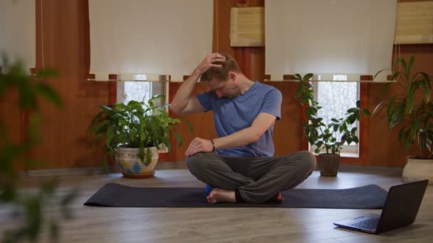 Athletic young male doing yoga exercises with online instructor using internet connection on laptop at home - Video, Çekim