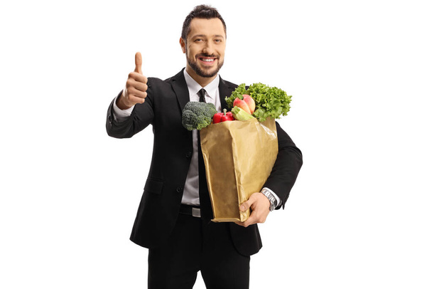 Young businessman with a grocery bag showing thumbs up isolated on white background - Fotó, kép