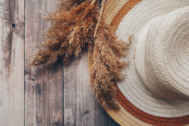 ψάθινο καφέ και μπεζ καπέλο και ξερά κλαδιά καλαμιών σε ξύλινο φόντο. Καλοκαιρινό καπέλο με σουτιέν. Υψηλής ποιότητας φωτογραφία - Φωτογραφία, εικόνα