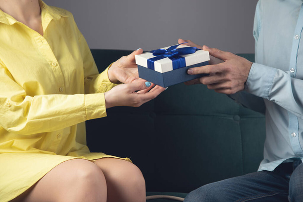 een man geeft een geschenk aan een vrouw die op een bank zit. het concept van een gezinsvakantie - Foto, afbeelding