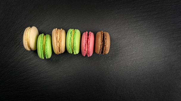 Multicolored macarons in a row on a black background with copy space - Foto, immagini