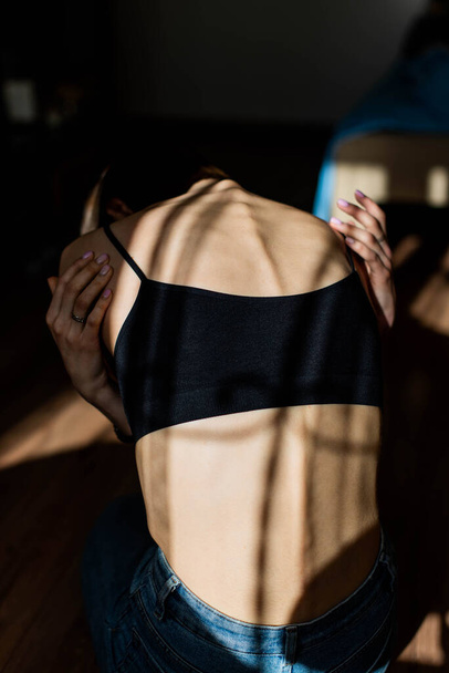 Een meisje met anorexia draaide zich om, ruggengraat en ribben zichtbaar. Jonge vrouw met anorexia zit alleen en voelt zich ongelukkig. Probleem met anorexia. - Foto, afbeelding