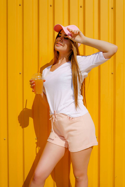 Pretty young hipster style girl have fun outdoor in white cap and eating ice cream on yellow background urban style - Φωτογραφία, εικόνα