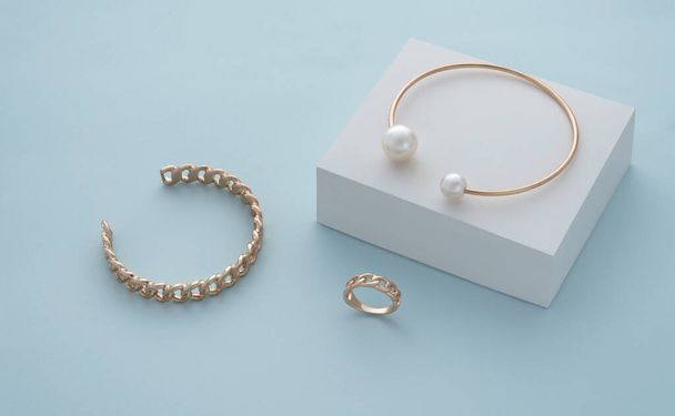 Golden pearl bracelet on white box and golden chain shape bracelet and ring on blue background - Fotó, kép