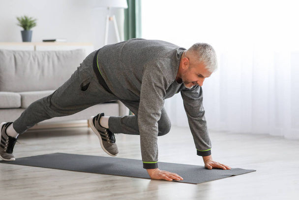 Athletic bearded senior man doing exercises at home - Foto, afbeelding