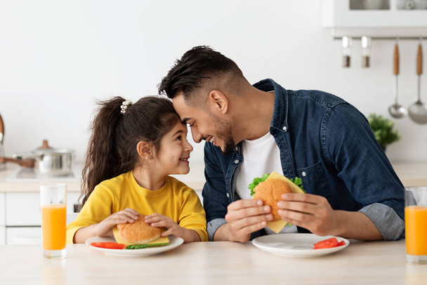 Happy Loving Arab Dad And Daughter Eating Sandwiches In Kitchen And Bonding - Photo, Image