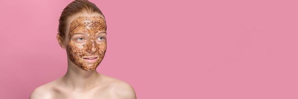 Facial skin scrub Coffee grounds mask on the face of a beautiful young woman Organic natural cosmetology Pink studio background Isolate - Photo, image