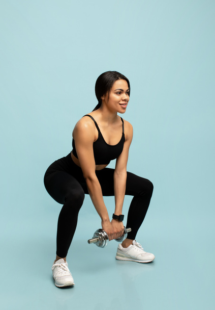 Νεαρή Αφροαμερικανίδα αθλήτρια γυμναστικής που κάνει ασκήσεις, κατάληψη με αλτήρα σε μπλε φόντο - Φωτογραφία, εικόνα