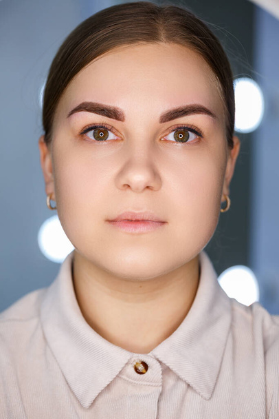 A close-up of the face of a young woman who has just had a permanent eyebrow tattoo done. - Fotó, kép