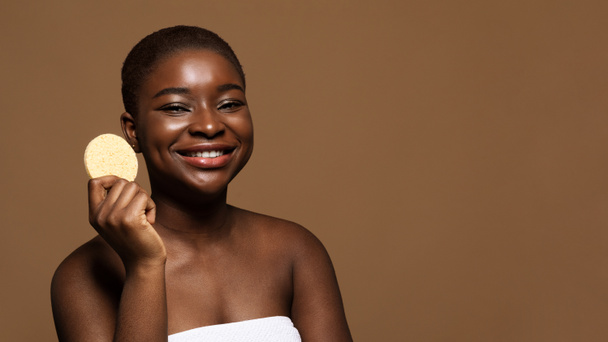 スキンケアコンセプト。顔のクレンジングのためのかわいいアフリカの女性保持化粧品スポンジ - 写真・画像