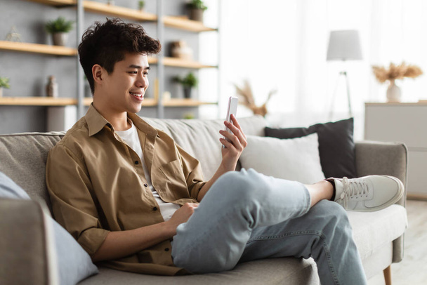 Primo piano di sorridente uomo asiatico utilizzando smartphone a casa - Foto, immagini