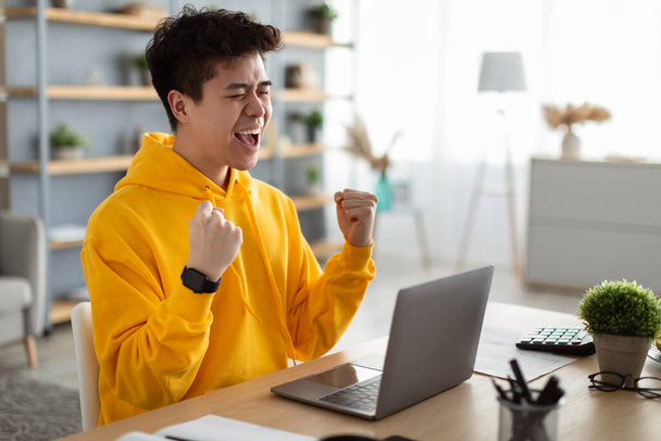 Asian guy using laptop celebrating success shaking fists - Фото, изображение