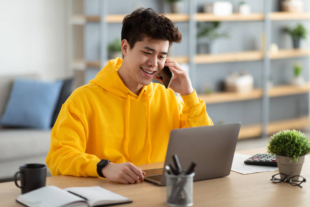 Sorridente uomo asiatico che lavora e parla al telefono a casa - Foto, immagini