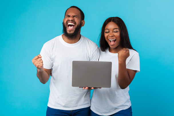 Black couple using laptop celebrating success shaking fists - Foto, Imagem