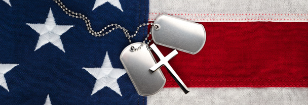 US military soldier's dog tags, rough and worn with blank space for text, and Christian cross necklace on American flag. Memorial Day or Veterans Day concept. - Photo, Image