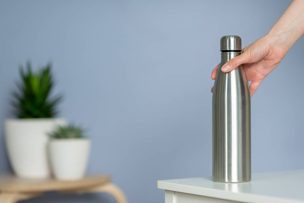 Woman hold steel water bottle on the table at home. Zero - 写真・画像