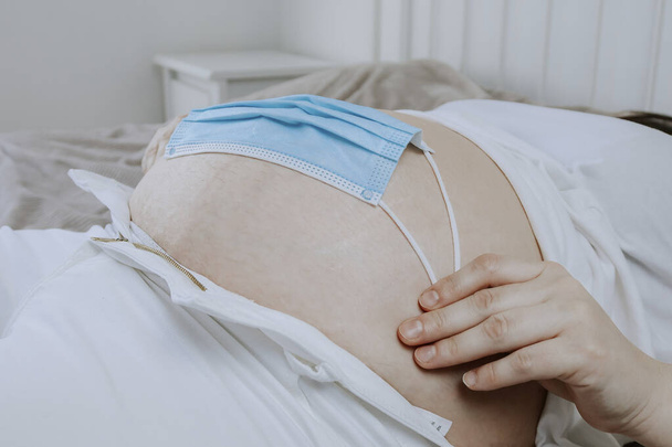 Une femme enceinte tient un masque sur le ventre, vue latérale rapprochée. - Photo, image