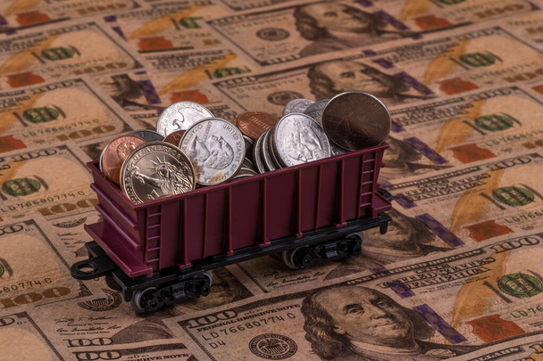 Un coche de carga de juguete del ferrocarril infantil con varias monedas estadounidenses se encuentra en los billetes de $100 - Foto, Imagen