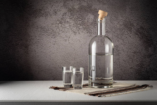 A glass bottle with glasses, a strong drink, on a white countertop against a gray wall - Foto, Imagen