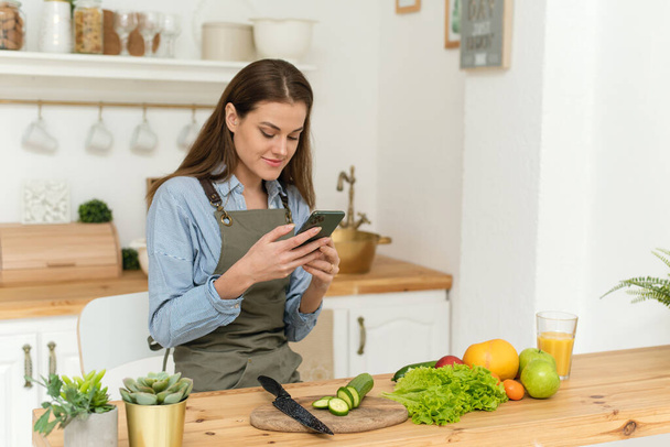 Giovane donna felice bere succo d'arancia e guardando attraverso le ricette sul suo smartphone. Insalata vegana. Dieta - Foto, immagini
