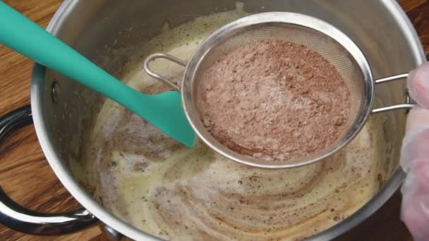 Egy lassított felvételen egy cukrász csokoládé habot készít, amit kakaóporral locsolnak. Az ember édes tésztával, szivacsos tortával és kakaós desszerttel dolgozik.. - Felvétel, videó