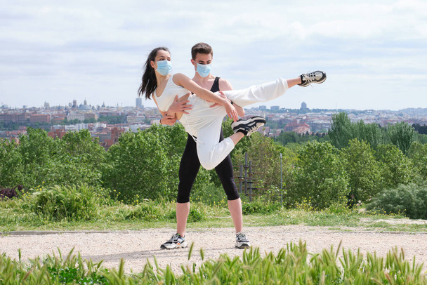 Nuori pari harjoittelee katutanssia, balettia, tanssiaskelia, liikkeitä puistossa suojaava kasvonaamio. - Valokuva, kuva