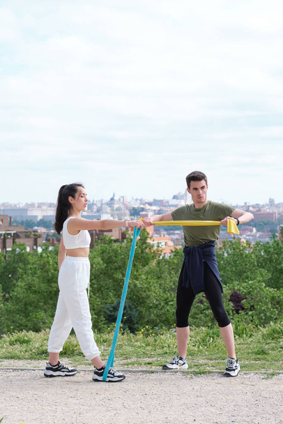 Young sporty couple exercising with rubber bands outdoors. Stretching exercises with elastic bands. - Photo, Image