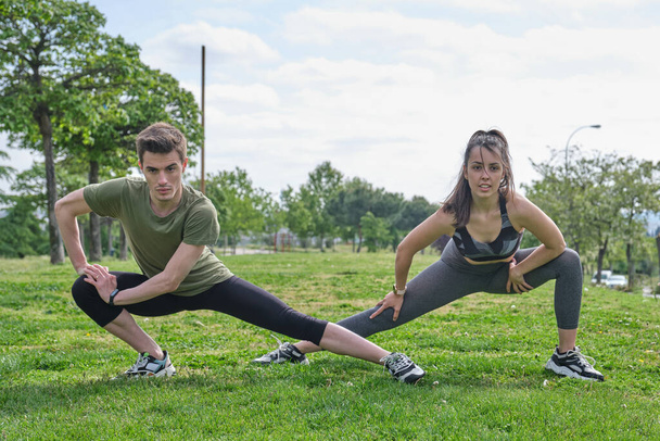 Young sporty couple stretching outdoors on the grass. Fitness concept. - Foto, Bild