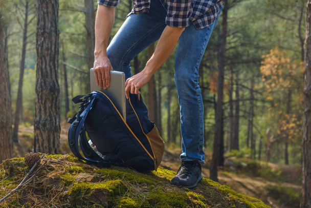 Cropped photography of young man getting laptop from the backpack at the forest - Φωτογραφία, εικόνα