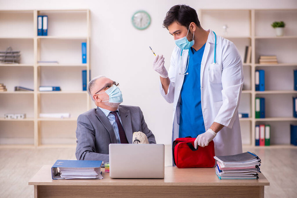 Young male doctor visiting old businessman at workplace - Photo, Image