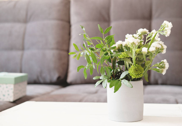 cement vase with green and white flowers on a table beside a sofa . trendy scandinavian style living room interior. simple home decor, contemporary room. - Fotografie, Obrázek
