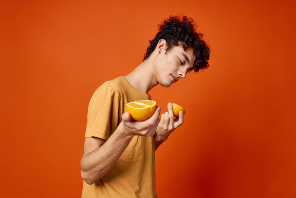 парень с вьющимися волосами апельсины в руках фруктово-красный фон - Фото, изображение