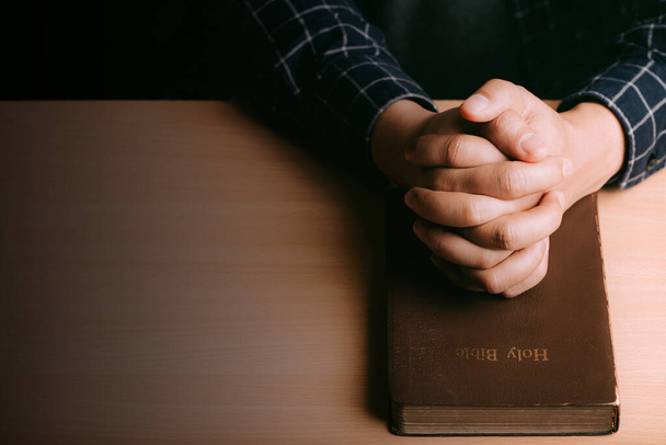 Hands of praying young man and Bible on a wooden desk background.man join hands to pray and seek the blessings of God, the Holy Bible.  - Foto, imagen