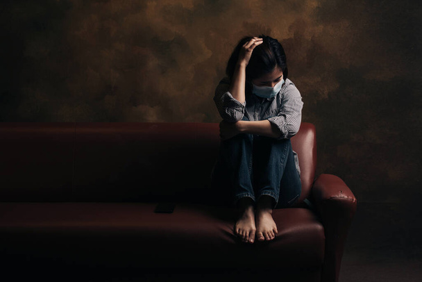 Yüzünde maske olan bir kadın sofada otururken kafasını kaşıyor. COVID-19 ile ilgili depresyon. - Fotoğraf, Görsel