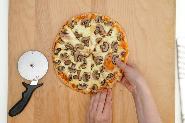 Pizza de champiñones Crimini con queso Mozzarella y salsa de tomate de cerca sobre tabla de madera, puesta plana, manos de mujer - Foto, Imagen