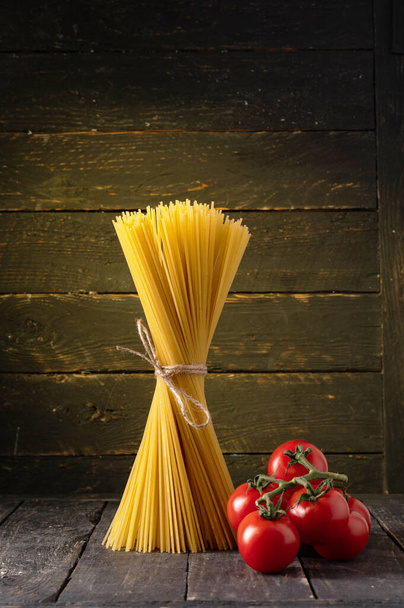 Spaghetti and cherry tomatoes. Pasta and tomatoes on a black background. Vertical frame. - Photo, Image