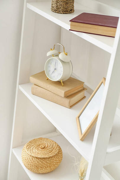 Shelves with alarm clock and decor near white wall - Foto, Imagem
