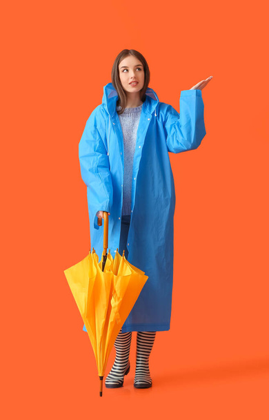 Stylish young woman in raincoat and with umbrella on color background - Valokuva, kuva